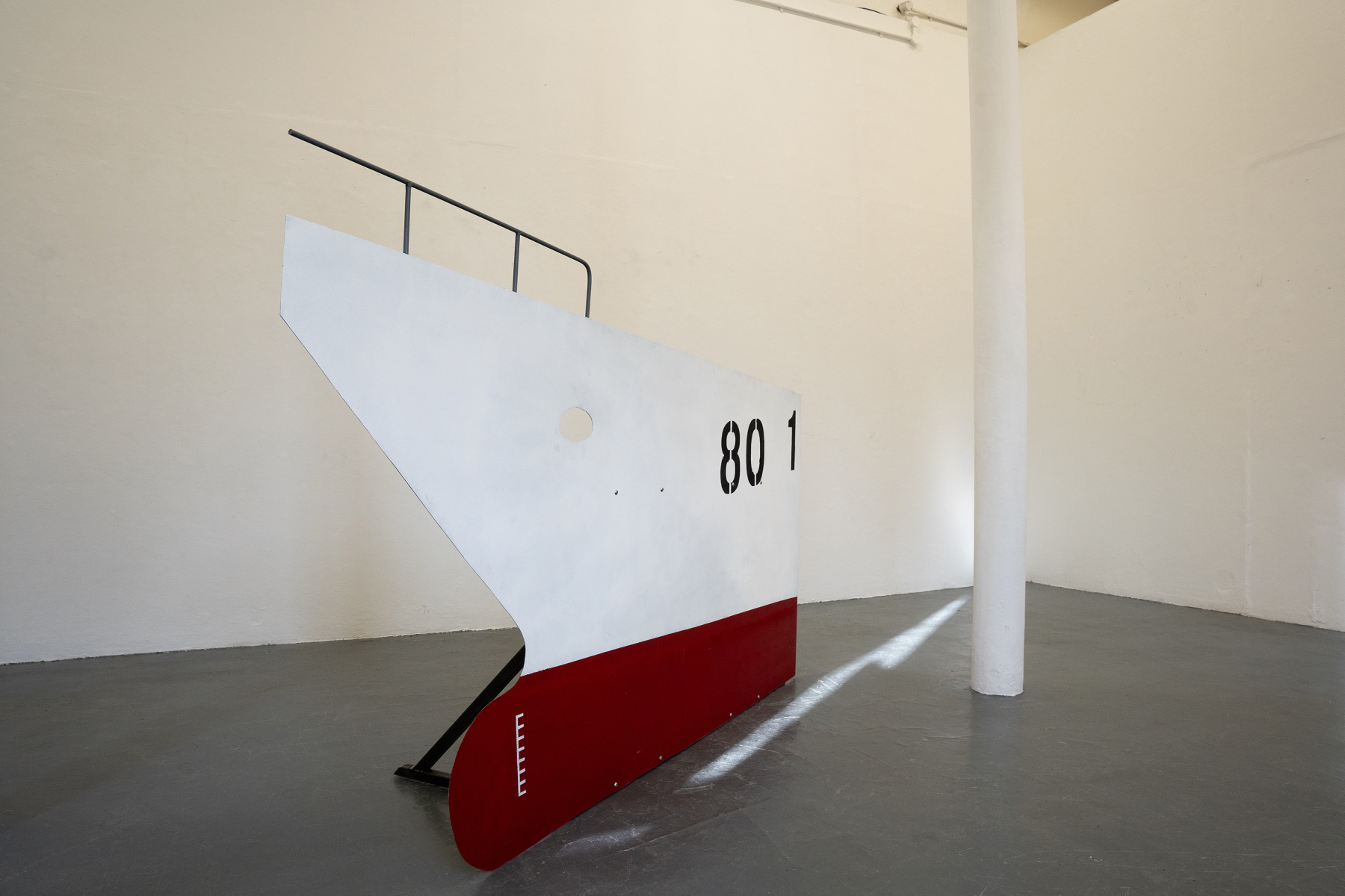 Installation photo of sculpture of part of ship's prow cut from steel sheeting, red at the bottom and white on the top. with the number "801" on one side