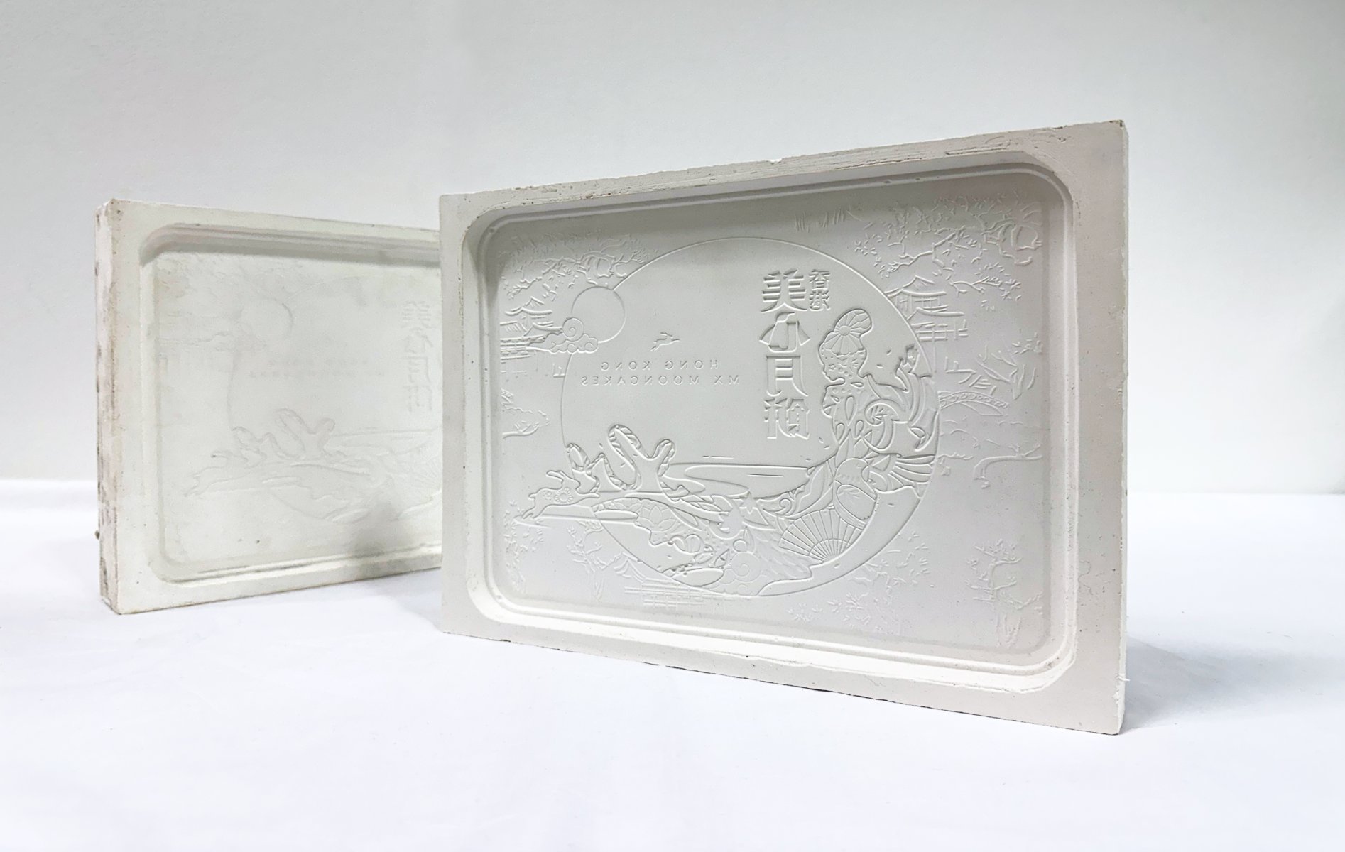 Two plaster casts of a moon cake tin with detailed and intricate patterning cast into the plaster. The words 'Hong Kong Mooncakes are printed backwards'