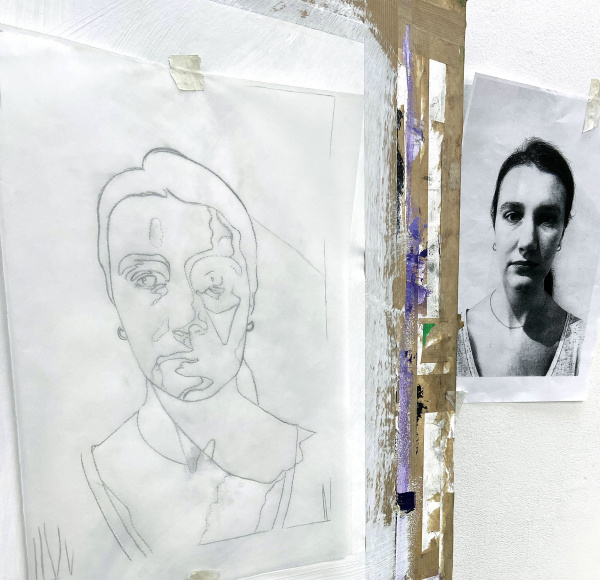 Easel with line drawing of face, next to a black and white photo of face.