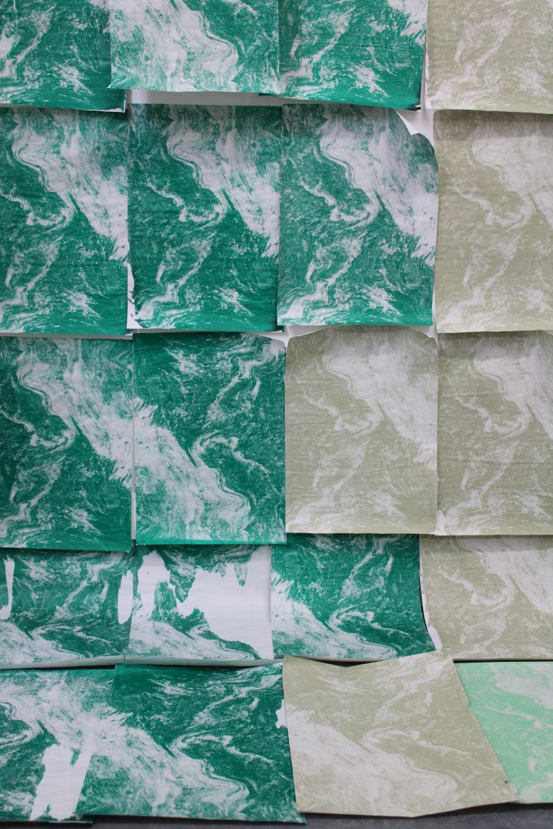 Close up of artwork made from rectangles of screenprinted newsprint, half viridian green and white, the other a light green-beige and white, loosely attached to paper(?)