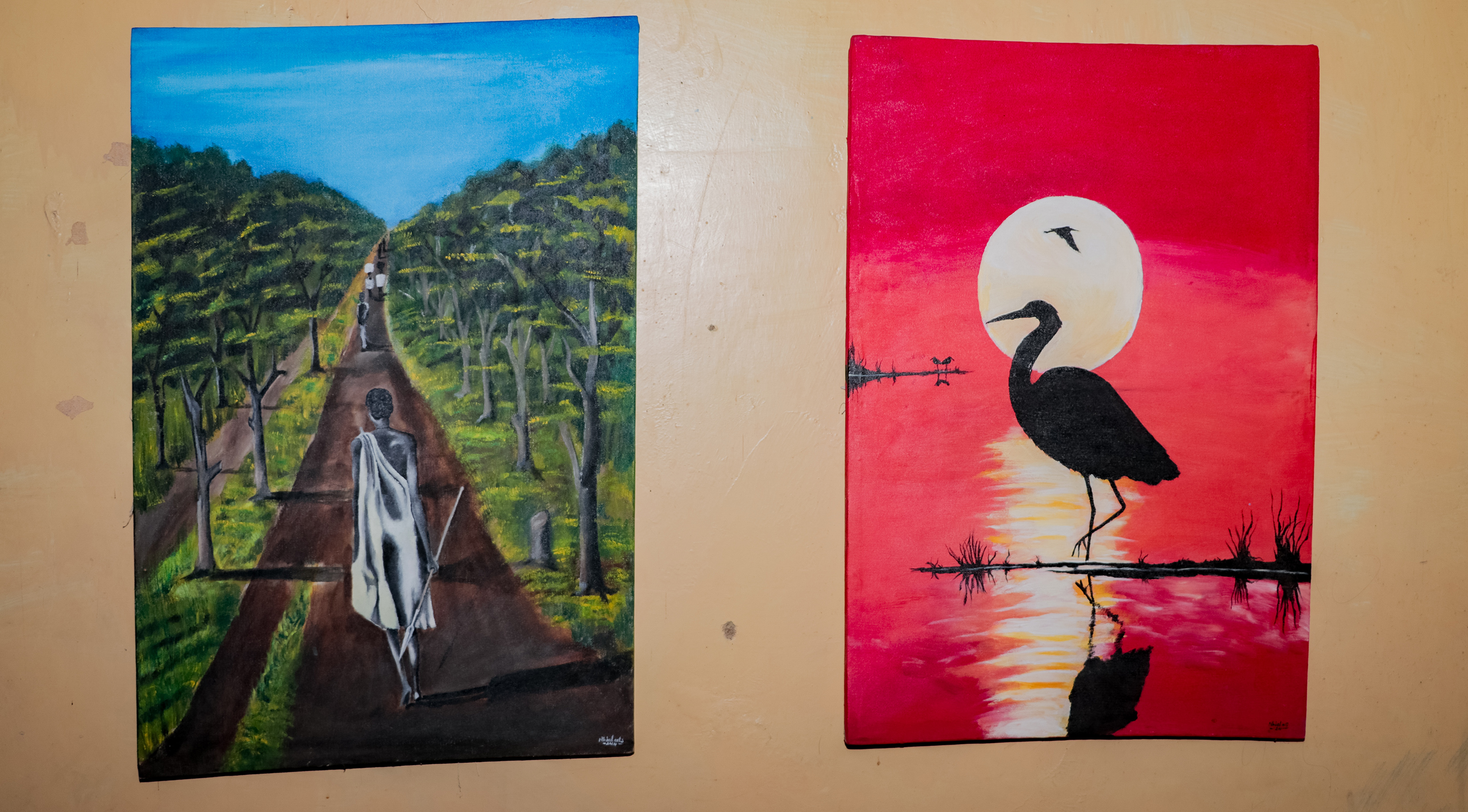 Two paintings: Village Souls of Harmony, showing a figure walking down a path trees on either side of him. The other Evening Grace shows a bird in silhouette against a sun in the red sky.